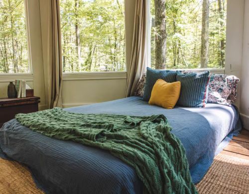 A mattress on the floor of a bedroom with blue bedding, a green blanket, and a yellow pillow.