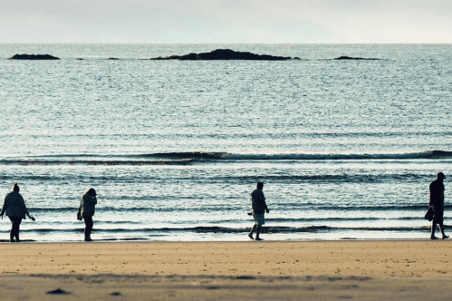 Four people walk along the shore at Hampton Beach in Hampton, New Hampshire.