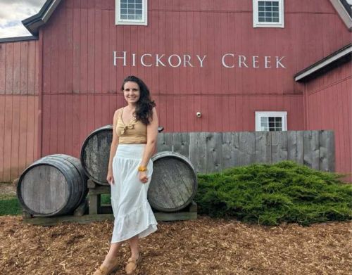 A woman standing in front of a red barn that says Hickory Creek.