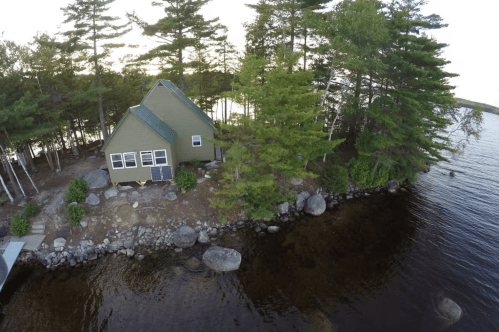 An aerial view of the Private Island With Rustic Cabin Airbnb rental in Indian Purchase Township, Maine. The rustic cabin sits on an island surrounded by a lake.