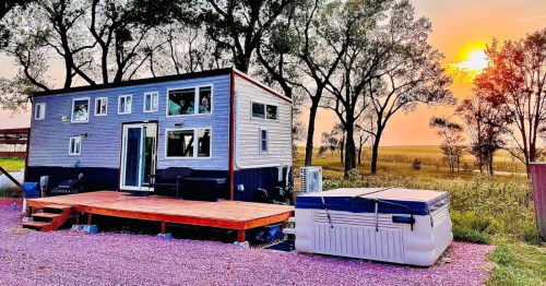 A tiny house Airbnb sits on the Nebraska prairie with a fiery sunset in the background.