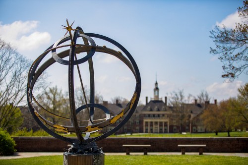 Sun dial in front of a college campus lawn and building
