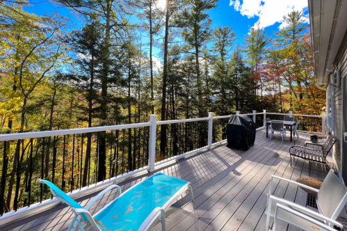 Large outdoor deck with a grill and dining table, overlooking a forest with fall foliage.