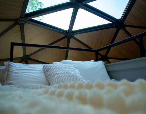 A bed with a white comforter in the loft of a glamping dome.