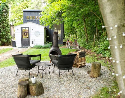 An outdoor fire pit with seating in front of a white tiny home.