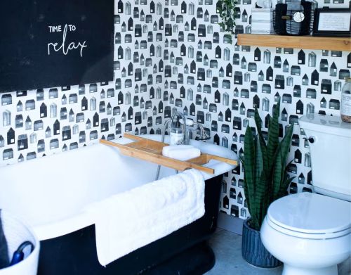 A black cast-iron bathtub in a restroom with black and white wallpaper.