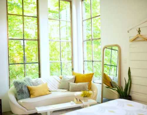 A living area with a white couch and colorful pillows in front of tall glass windows.