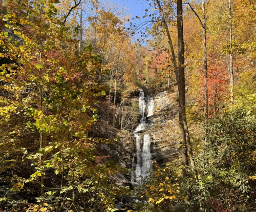 A multi-tiered waterfall emergences from a thick forest in fall colors.