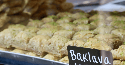 A bakery tray filled with rows of baklava, topped with a sign that reads "Baklava."
