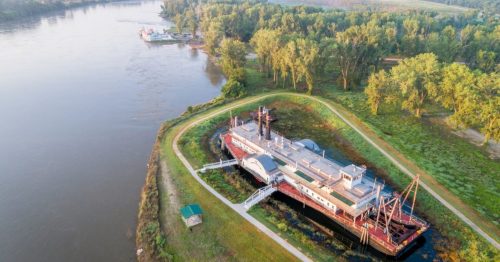 A red and white riverboat permanently docked in the green grass to the right of the Missouri River