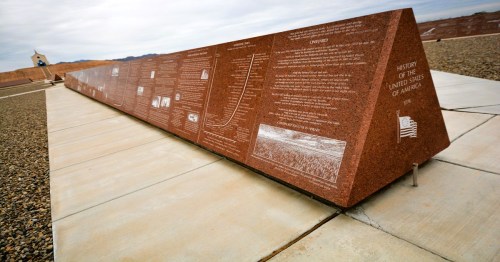 A massive, triangular granite monument carved with historical text and diagrams at a quirky roadside attraction in Southern California.