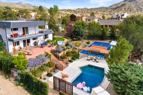 An aerial view of a resort-style Airbnb in New Mexico featuring a swimming pool with inflatable swans, a pickleball court, a hot tub, and a large furnished patio surrounded by lovely gardens.