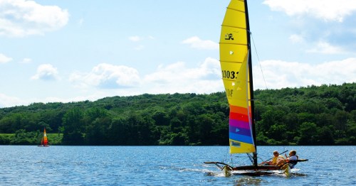 A catamaran with a bright yellow sail is drifting on a scenic lake in Pennsylvania