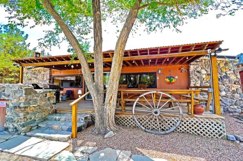 A Southwestern-themed Airbnb in Nevada, with stone accents, wagon wheel decor, a wooden covered porch, and a large tree in the front.