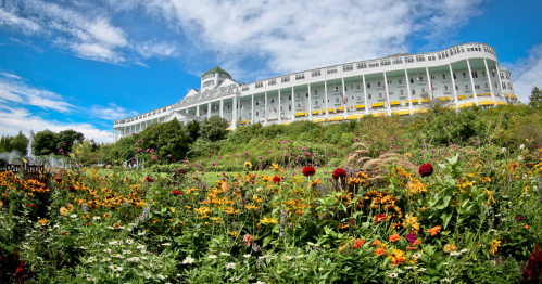 Bright green plants and yellow, red, and orange flowers in the foreground with the bright white Grand Hotel in the background beneath a blue sky with puffy white clouds