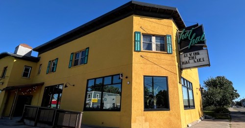 A vibrant yellow building with large windows and a neon sign reading "Living the Hat Life."