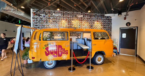 a vintage-style yellow schoolbus with words "the joy bus diner" painted in red on the side, its door open revealing a dining table with bench seating in phoenix, arizona