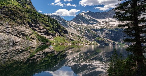 a gorgeous view of a mountain covered in forest trees and a sparkling lake below and cloudy sky above