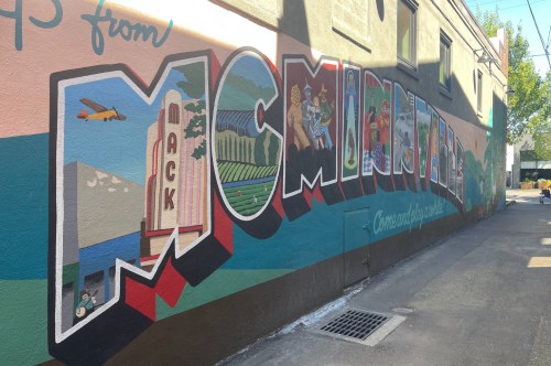 A painted wall mural that reads 'Greetings from McMinnville' with the letters of McMinnville in bubble letters with images painted inside.