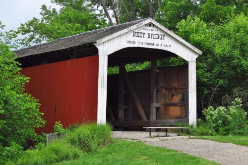 A historic covered bridge surrounded by greenery, with a sign reading "1906" and "Cross this bridge at a walk." Image source: https://flic.kr/p/2mZEahP