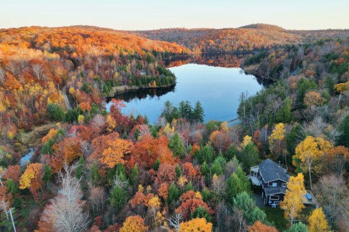 An aerial view of the Lakefront Otis Home VRBO property in Otis, Massachusetts. Vibrant fall foliage surrounds the home and nearby Hayes Pond.
