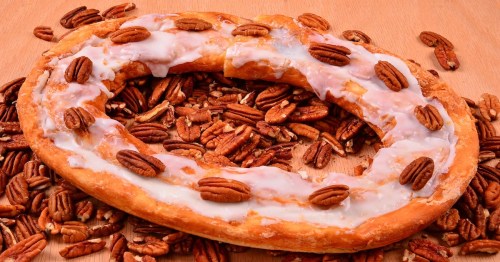 A kringle covered in frosting and pecans on a bed of pecans