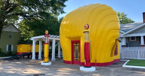 A roadside attraction in Winston-Salem, NC, housed in a bright yellow seashell-shaped building, featuring old-fashioned gas pumps.