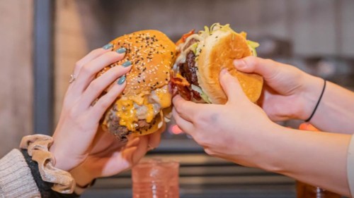 Two hands holding big, overflowing burgers "cheers"