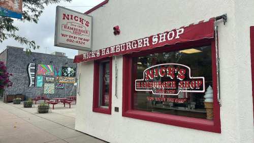 White and red building with "Nick's Hamburger Shop" in old timey lettering