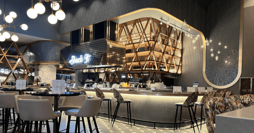 The bar area at Alto Steakhouse with stools and brightly lit bar shelving