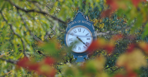 A street clock for the "Town of Bethel, 1796" is seen through a soft focus of autumn leaves.