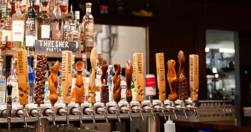 A draft beer tap with many handles and bottles of alcohol in the background.