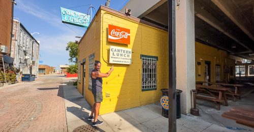 Man standing outside a yellow concrete block building, the Canteen Lunch Box in Ottumwa Iowa