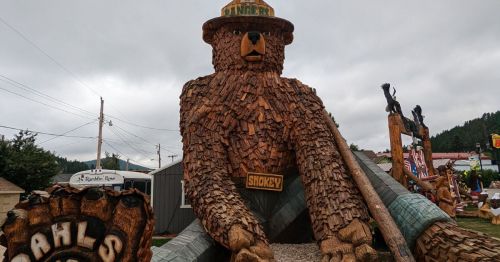 A giant wood-carved sculpture of a bear wearing a hat and jeans.