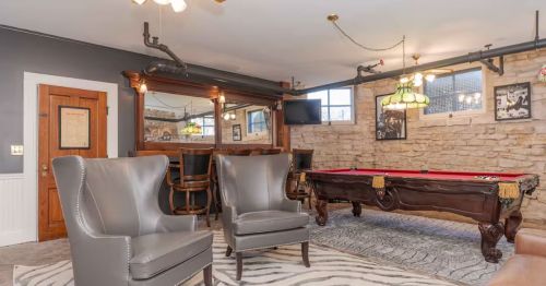 A basement with a brick wall, two gray chairs and a pool table.