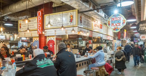 A group of people sitting at the counter of a food hall stand called Dutch Eating Place.