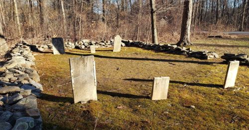 A small cemetery surrounded by a rock wall in a forest.