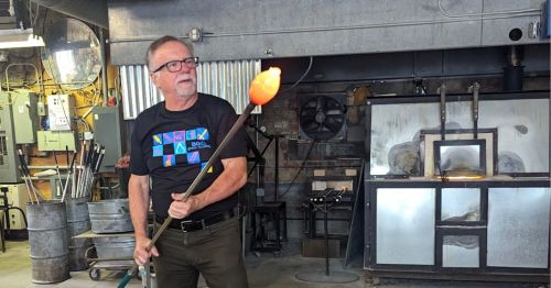 A man holding up tools to demonstrate glass blowing.