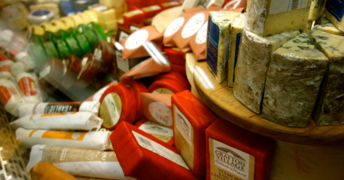 A wide variety of artisanal cheeses on display, including rounds of Grafton Village Cheddar with red wax.