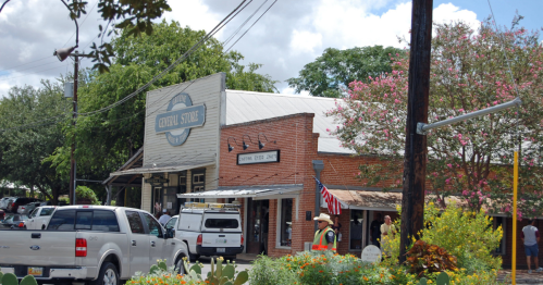 Visitors explore the Gruene General Store and Cotton Eyed Joe’s on a sunny day, surrounded by blooming trees and local charm.
