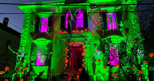 A house decorated for Halloween in Salem with bright green and purple lights, skeletons, and pumpkins.