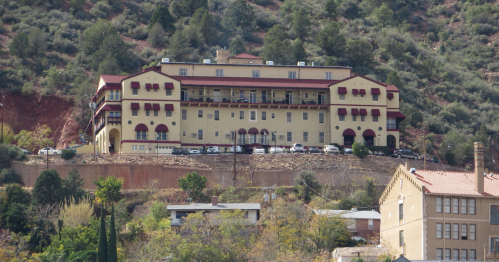 Historic Jerome Grand Hotel in Arizona perched on a hillside with red rock cliffs and green trees.