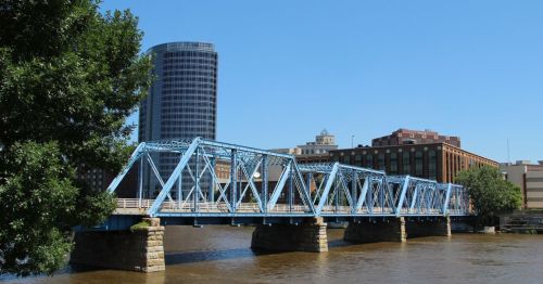 A blue bridge is going over a river with a tall building behind it.
