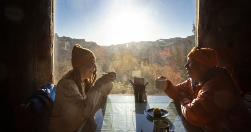 Two people drinking coffee at a table next to a window that has views of rock formations.