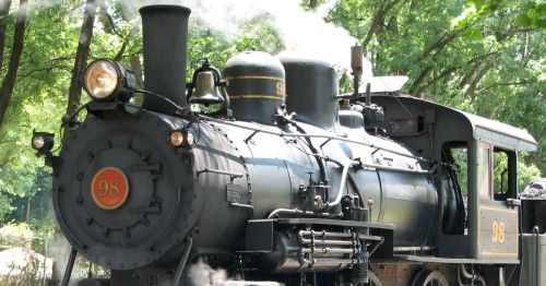 An old black train blowing steam.