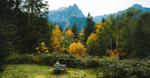 A woman sits on a picnic table while surrounded by trees on an autumn day. Index Mountain is visible in the background.