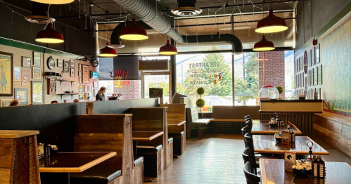 The interior of a restaurant with wooden booths, large windows, and walls covered in artwork.