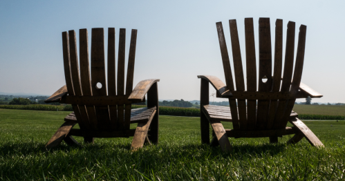 Two empty Adirondack chairs on a grassy hill overlooking the fields and vineyards of Waltz Vineyards in Manheim, PA.