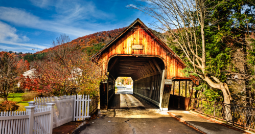 Middle Covered Bridge in Woodstock, Vermont, with fall foliage, a white fence, and a sunny sky.