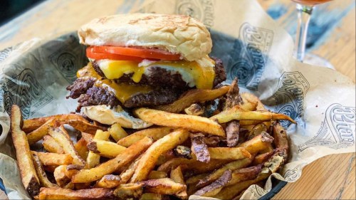 A basket filled with french fries and a double cheeseburger with all the fixings